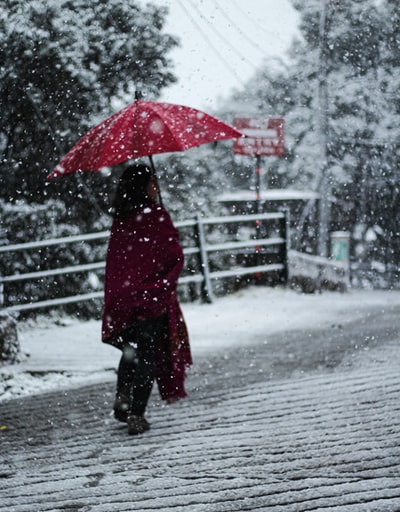 红袄的女人拿着雨伞站在冰雪覆盖的地面白天
